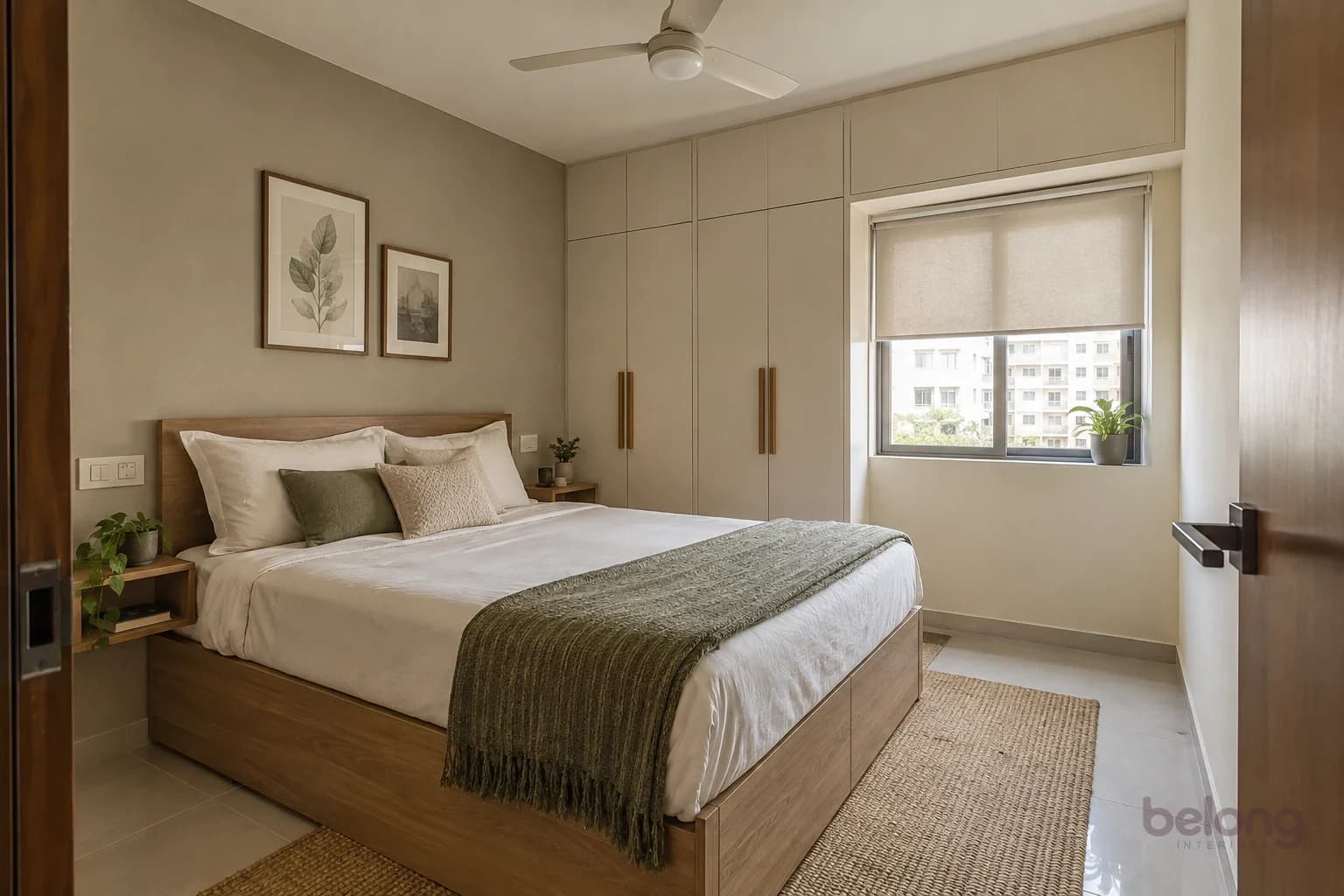 A calm bedroom with an ash-wood storage bed, white cotton bedding and a green throw, two small framed prints and floor-to-ceiling cream wardrobes with slim wooden pulls.