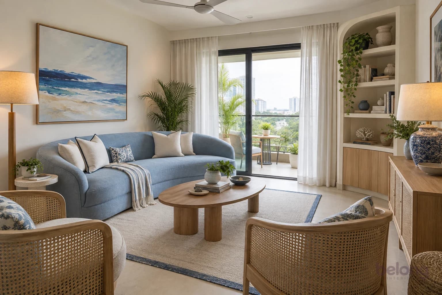 Living room with a powder-blue curved sofa, white cushions with navy piping, an oval oak coffee table, two cane chairs and a cream rug with a blue edge on pale floor tiles.