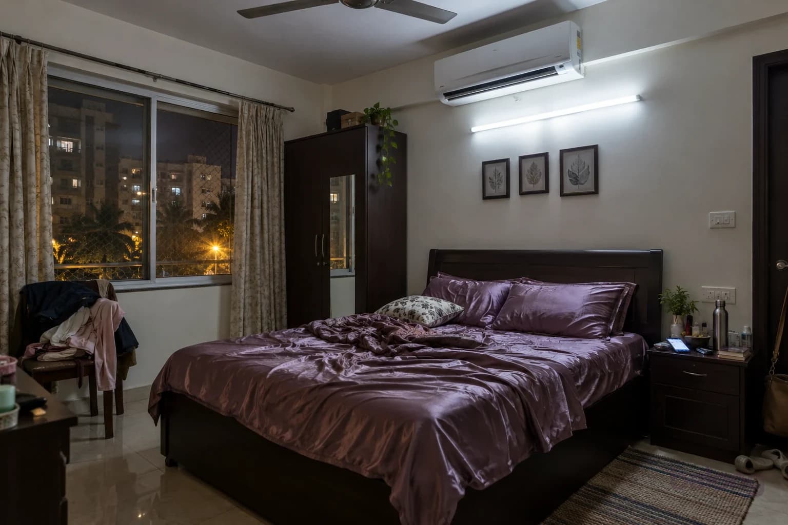 An ordinary bedroom before: a bright tube light, thin curtains, an AC pointed at the bed, clothes on a chair and a cluttered side table.