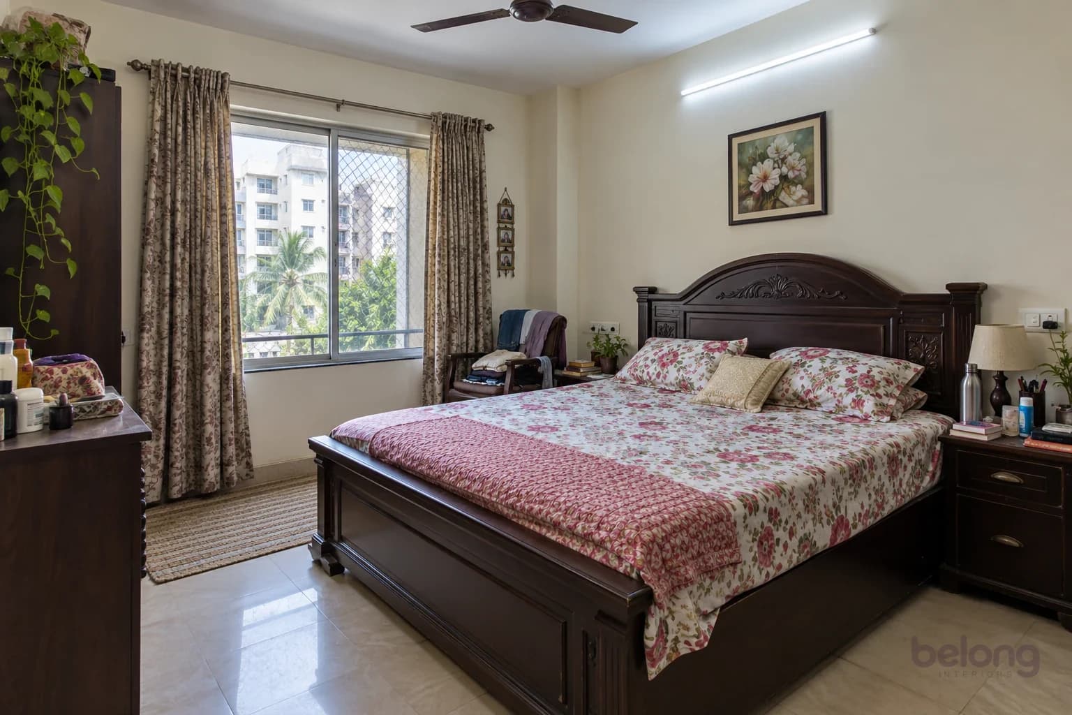 An ordinary apartment bedroom before: a heavy dark bed, busy printed bedding, a crowded side table and clothes on a chair.