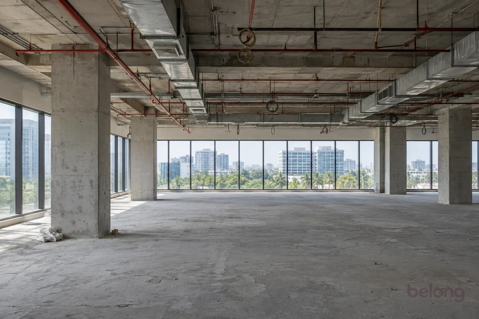 An empty office floor before fit-out: bare concrete, exposed ducts and columns, and rows of windows.
