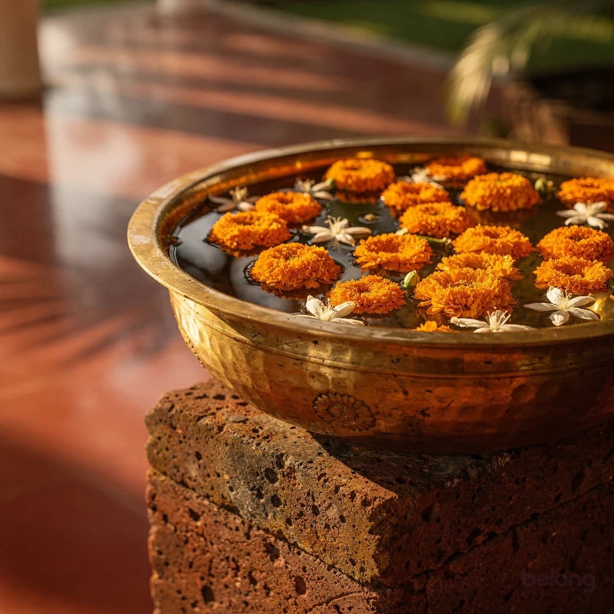 A brass urli of floating marigolds on a laterite plinth
