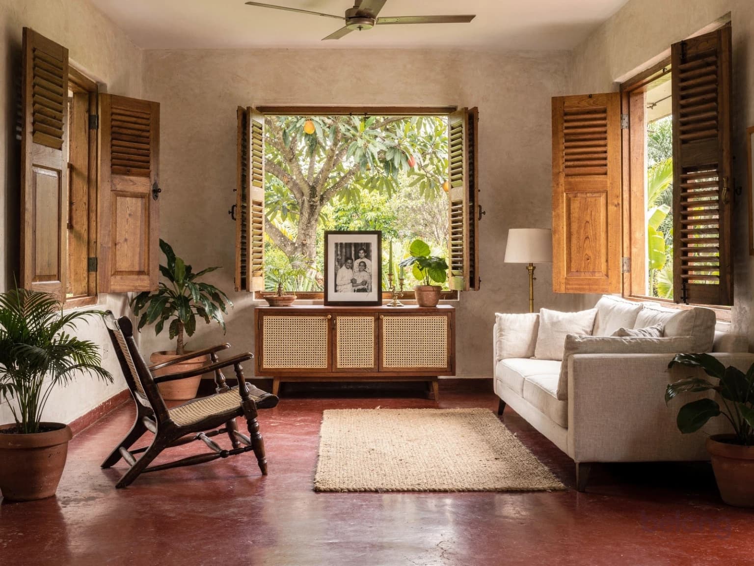 An older home’s living room with its red-oxide floor and teak shutters restored