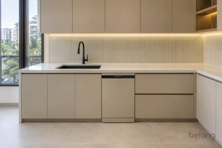 Black composite undermount sink with a matte-black faucet in a compact sand-coloured kitchen.