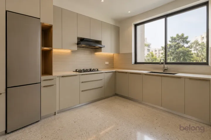 New modern compact L-shaped kitchen in oatmeal and brushed bronze, with warm ivory sintered stone worktops and slim horizontal oatmeal ceramic tiles.