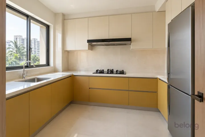 Small L-shaped kitchen with muted mustard lower cabinets, cream upper storage and a window over the sink.