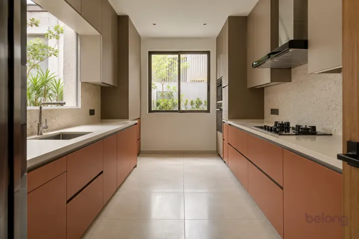 New modern parallel kitchen with a clear aisle in terracotta and warm taupe, with cream solid surface worktops and very pale beige fine-speckle terrazzo backsplash.
