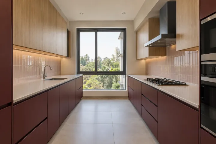 New modern parallel kitchen with a clear aisle in burgundy and pale oak, with warm-white solid surface worktops and pale blush rectangular tiles in stacked rows.