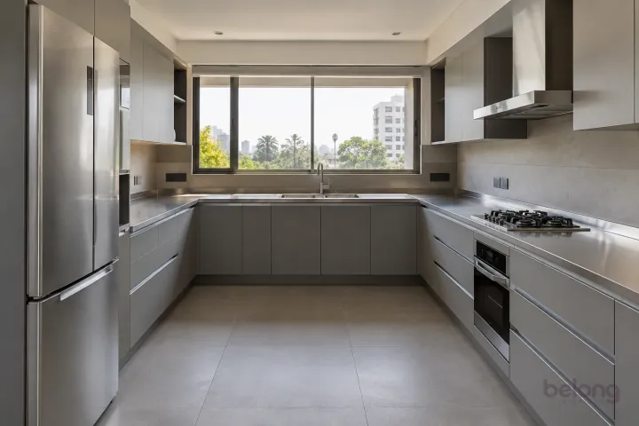 New modern generous U-shaped kitchen in concrete grey and satin steel, with brushed stainless steel worktops and warm grey large-format porcelain.