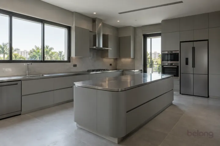 New modern villa kitchen with a central island in concrete grey and satin steel, with brushed stainless steel worktops and warm grey large-format porcelain.