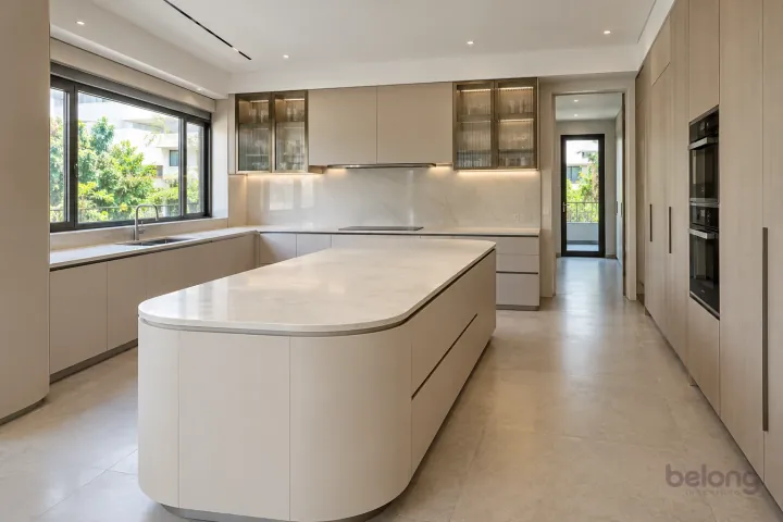 Sculptural ivory villa kitchen with a rounded-end island and slim framed ribbed-glass cupboards.