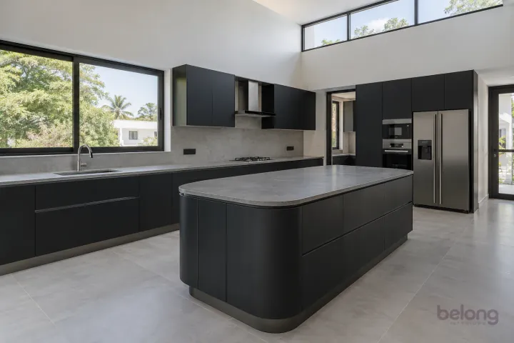 New modern villa kitchen with a central island in matte black and slate, with honed grey porcelain worktops and pale concrete-look slab backsplash.