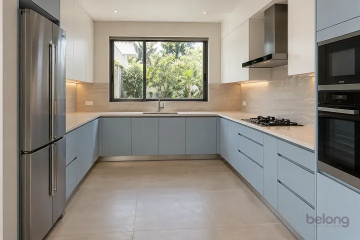 New modern generous U-shaped kitchen in dove blue and pale stone, with ivory quartz worktops and travertine-look porcelain slab.