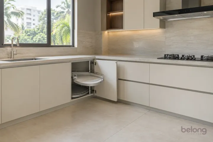 New ivory corner cabinet with empty kidney-shaped swing-out shelves and pale stone counters.