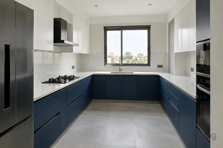 New modern generous U-shaped kitchen in ink blue and cloud white, with white quartz with sparse subtle grey veins worktops and large matte off-white ceramic rectangles.