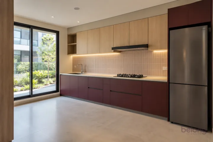 New modern compact straight kitchen in burgundy and pale oak, with warm-white solid surface worktops and pale blush rectangular tiles in stacked rows.