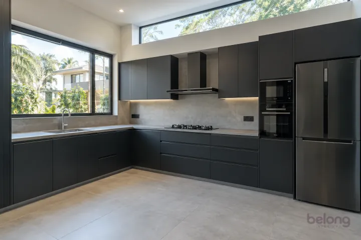 New modern compact L-shaped kitchen in matte black and slate, with honed grey porcelain worktops and pale concrete-look slab backsplash.
