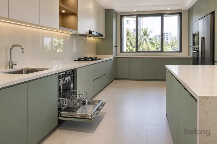 An open integrated dishwasher with clean empty racks beside the sink in a new sage kitchen.