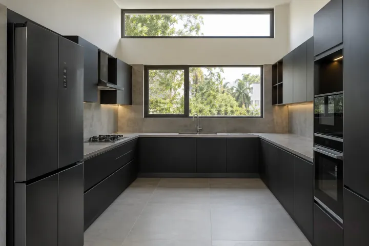 New modern generous U-shaped kitchen in matte black and slate, with honed grey porcelain worktops and pale concrete-look slab backsplash.