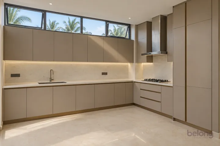 Taupe kitchen with a clerestory window above, with taupe and warm white stone finishes, precise fitted joinery and pristine surfaces in a contemporary Indian home.