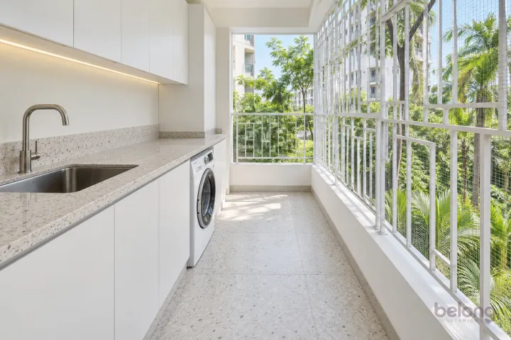 White utility balcony with a geometric grille, with bright white and light terrazzo finishes, precise fitted joinery and pristine surfaces in a contemporary Indian home.