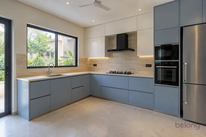 New modern compact L-shaped kitchen in dove blue and pale stone, with ivory quartz worktops and travertine-look porcelain slab.