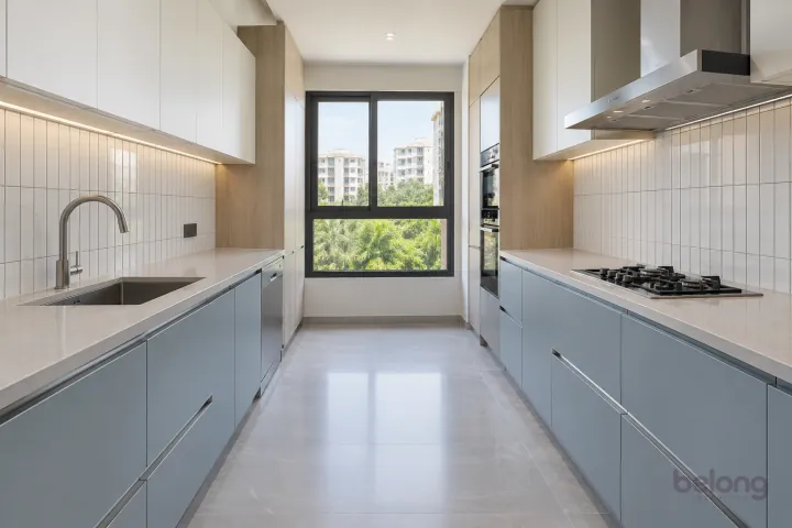 Parallel kitchen in powder blue and white with pale stone counters and a shaded end window.