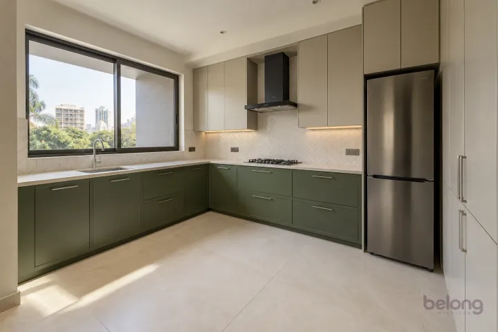 New modern compact L-shaped kitchen in moss green and greige, with pale beige sintered stone worktops and warm-white tile in a simple herringbone pattern.